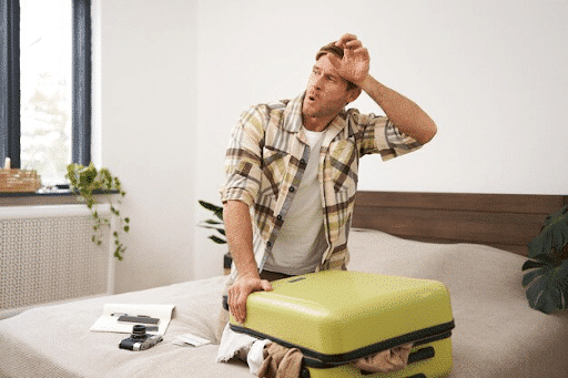 Man wiping sweat while packing suitcase on bed