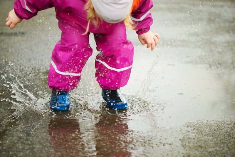 young girl jumping in a puddle of water