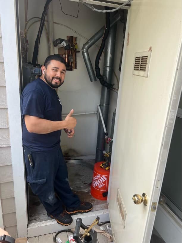 Technician giving thumbs up while servicing HVAC system in a utility closet