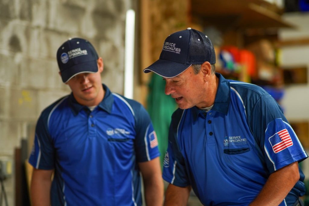 SS technicians in blue uniforms and caps discussing a task in a workshop