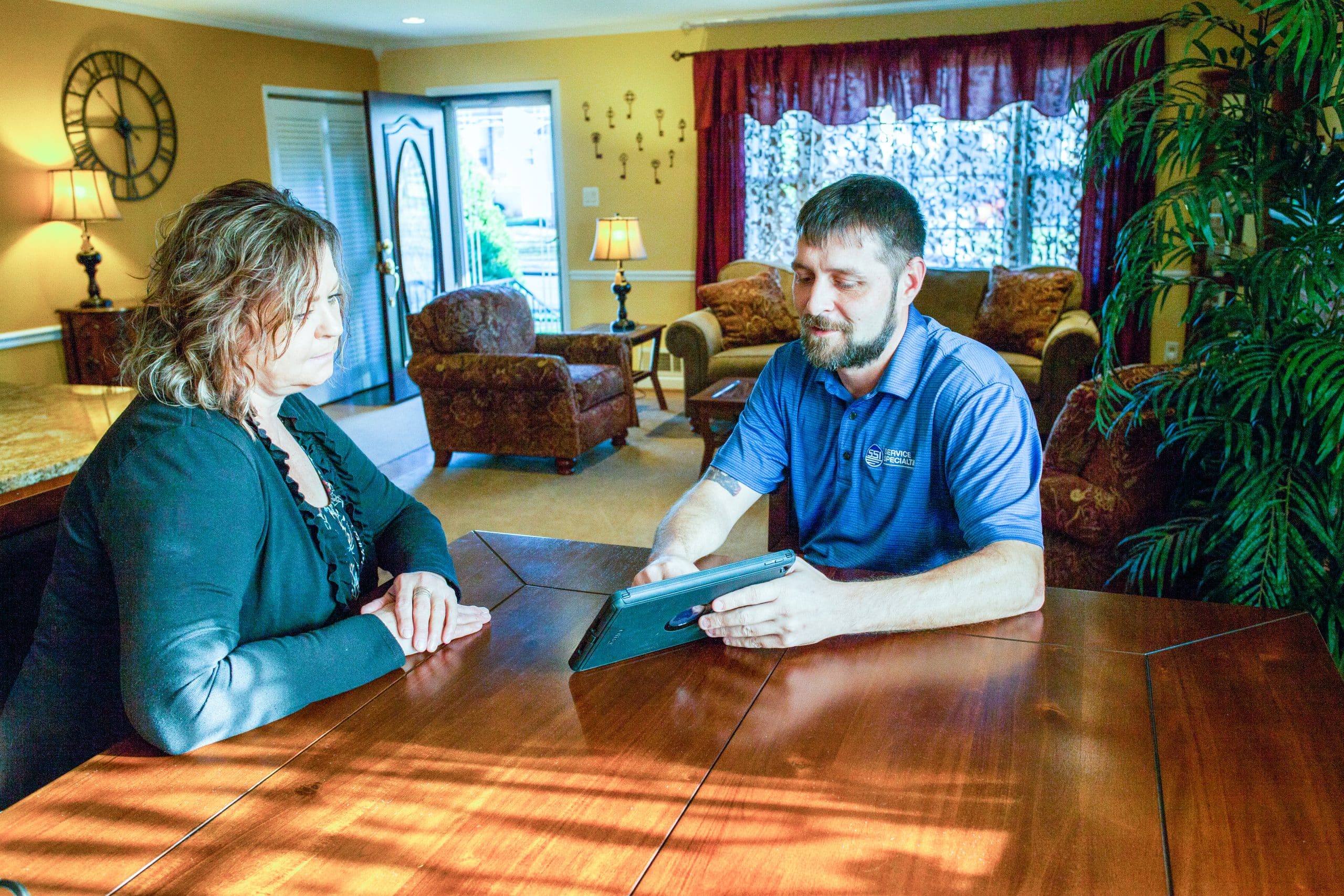 Technician in blue shirt discussing services with a customer at a wooden table