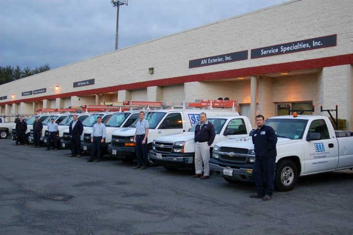 SS staff standing beside a fleet of white service trucks in a parking lot
