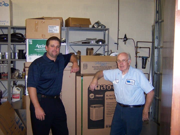 SS team members standing beside HVAC equipment boxes in a storage room