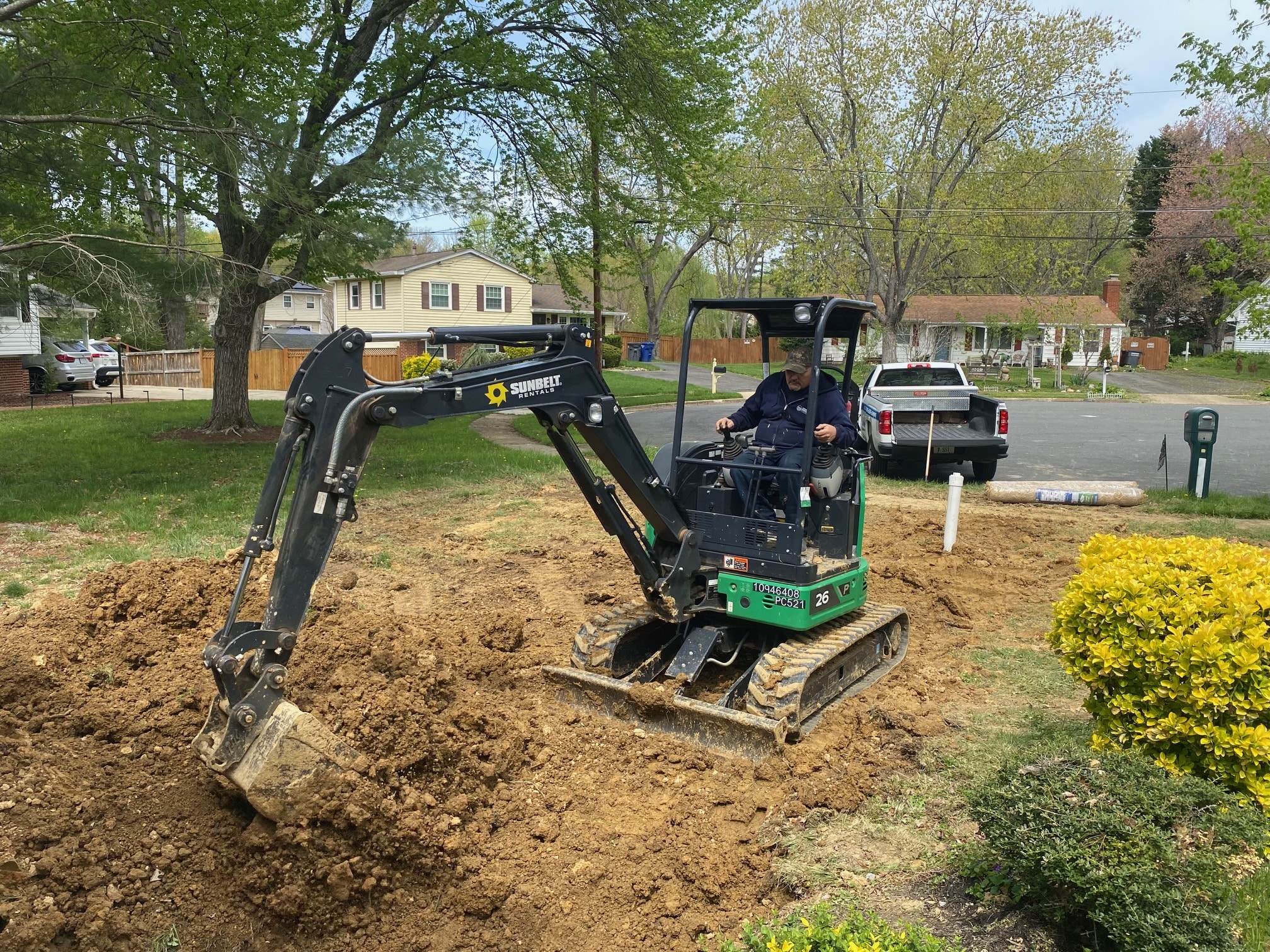 Technicians working in a deep trench on underground piping outside a house, with a mini excavator and PVC materials nearby