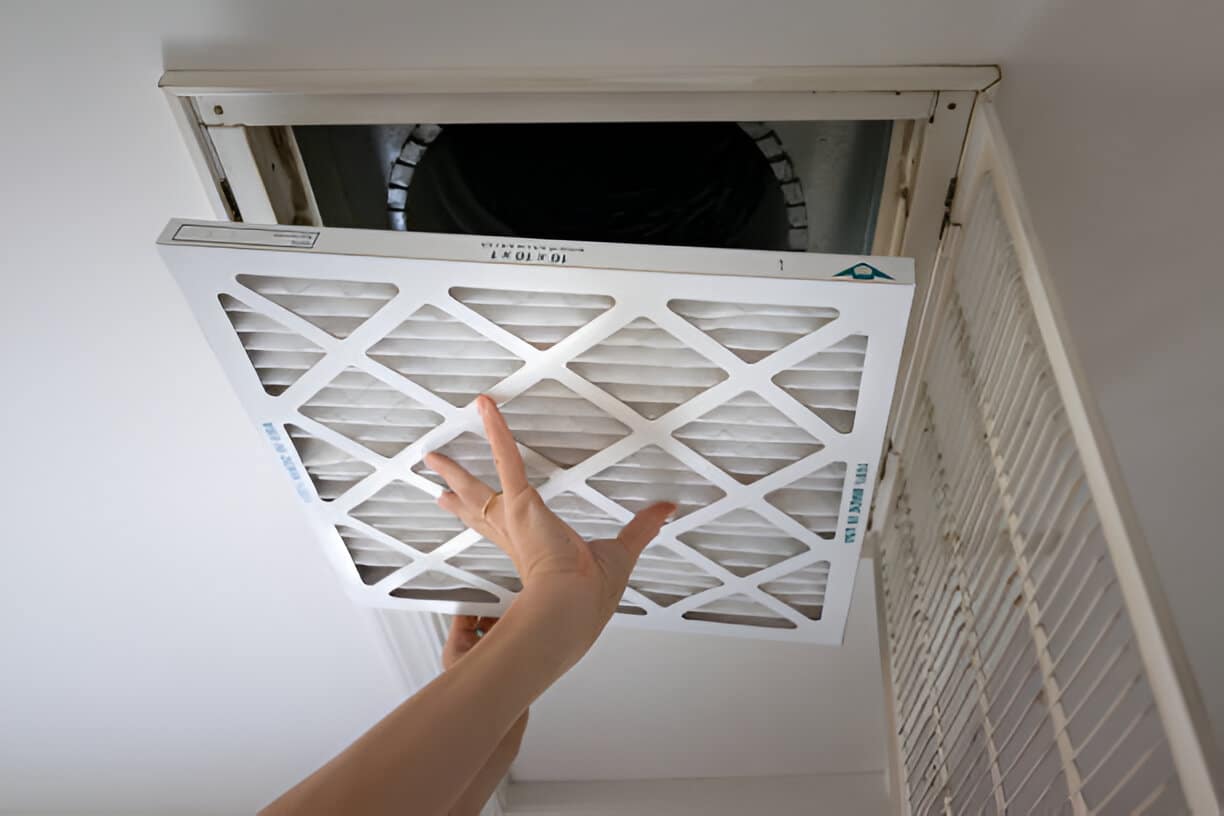 Person replacing an HVAC air filter in a ceiling vent
