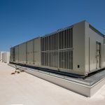 air handler installation stock photo Large commercial HVAC rooftop unit installed on a flat industrial building under clear blue sky.
