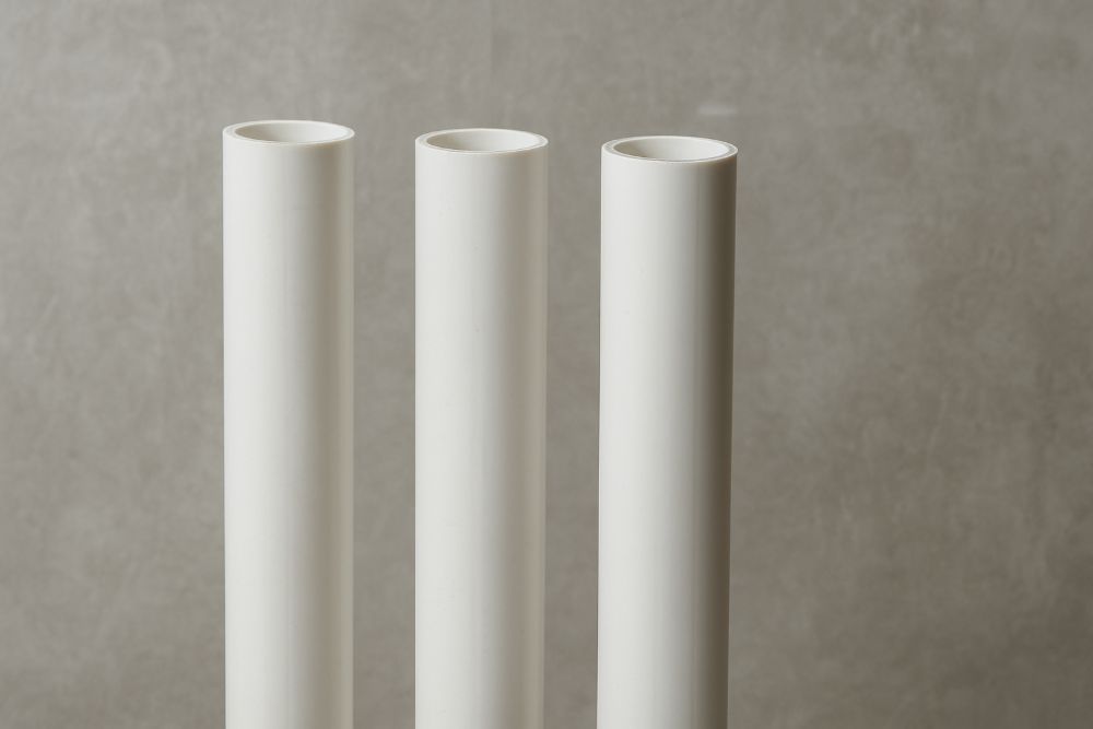 Three white PVC pipes standing vertically against a concrete background, commonly used in residential drainage systems and tools for plumbing.