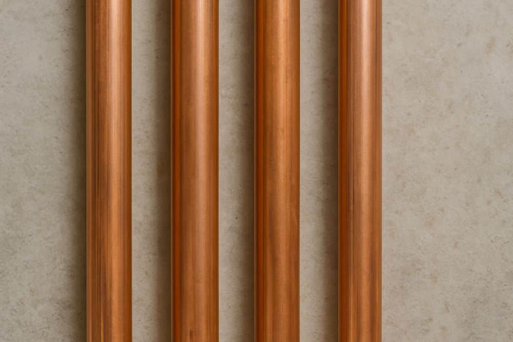 Four vertical copper pipes lined up against a concrete wall, commonly used in residential water lines and tools for plumbing.