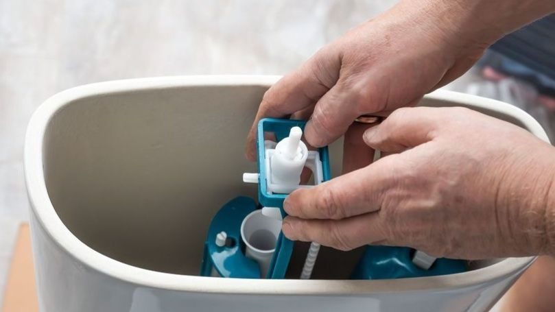 Plumber opening back of toilet to repair.